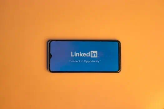LinkedIn logo displayed on smartphone screen over orange background, representing professional networking and online career opportunities.