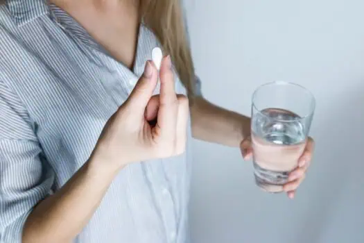 Hand holding a white pill and a glass of water, medication, pill intake, healthcare, medication management, woman taking medicine, health and wellness.