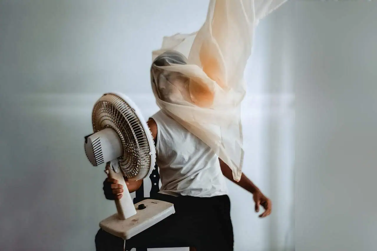 Fan holding person with fabric and steam, indoor setting, ambient light, modern lifestyle, emphasising comfort and cool airflow, promotional healthcare or wellness imagery.