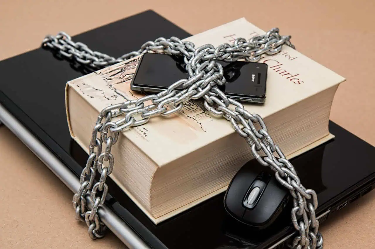 Chains wrapped around a book, smartphone, mouse, and laptop symbolising cyber security threats and digital privacy protection.