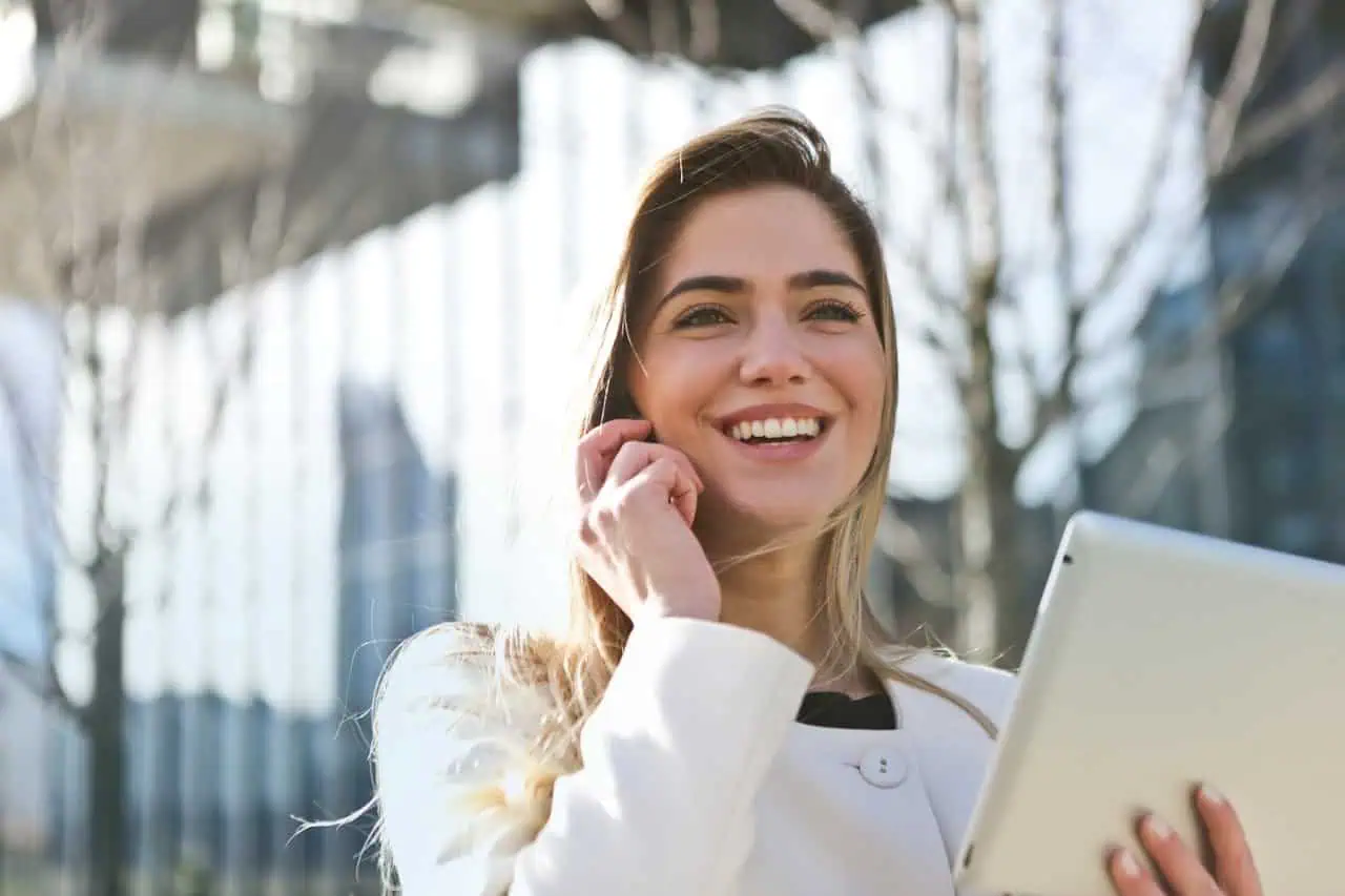 Smiling woman using a tablet outdoors in a modern urban setting, representing confidence, communication, and digital connectivity. Perfect for careers, personal development, or technological themes.