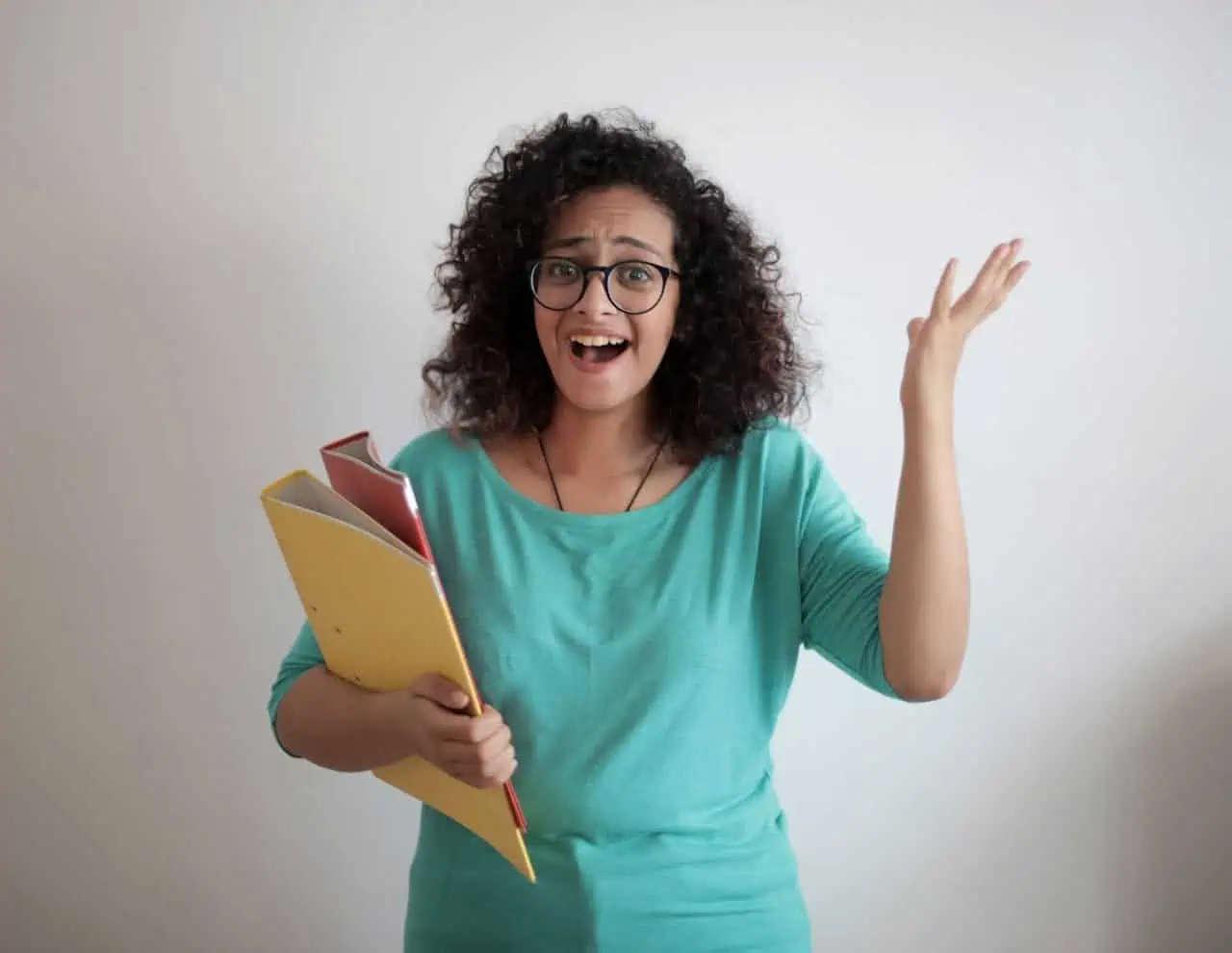 Frustrated woman holding folders and papers, expressing confusion or stress, wearing casual teal top, indoor setting, relevant to education, office work, or personal organisation.