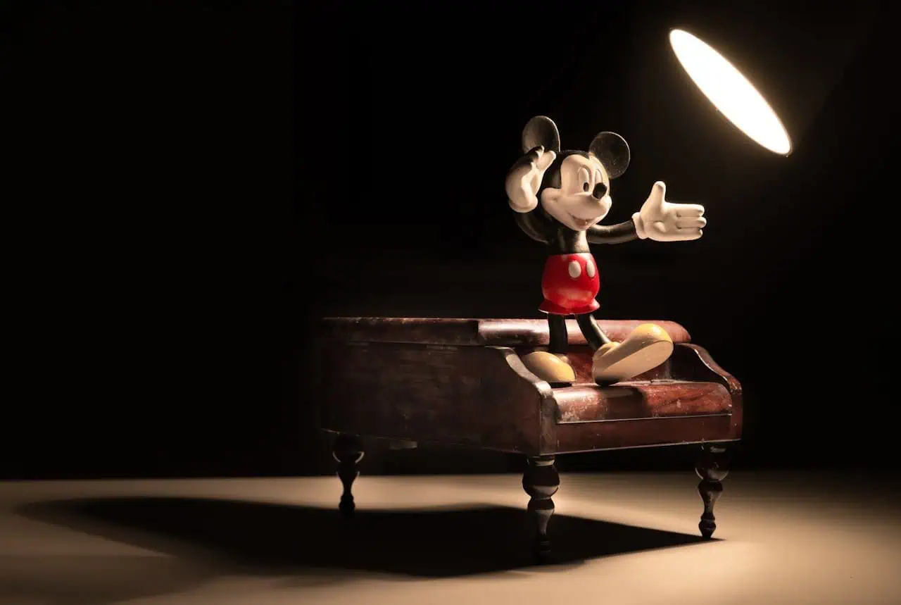 A close-up of Mickey Mouse figurine standing on a vintage wooden table with spotlight.