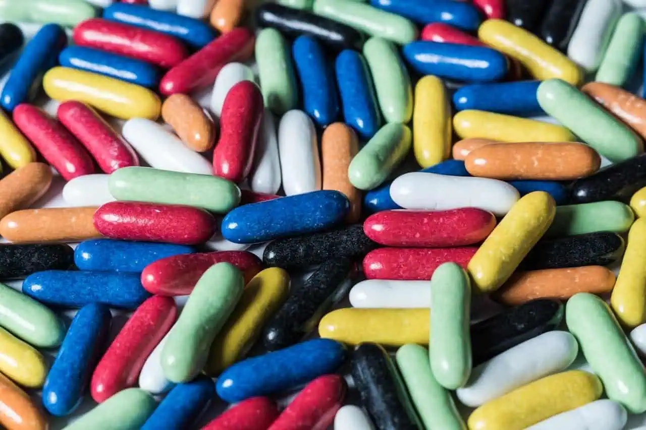 Colourful jelly beans in various shades including red, green, blue, white, black, yellow, orange, and pink, scattered together. Bright candy treats ideal for snacking or decorating desserts.