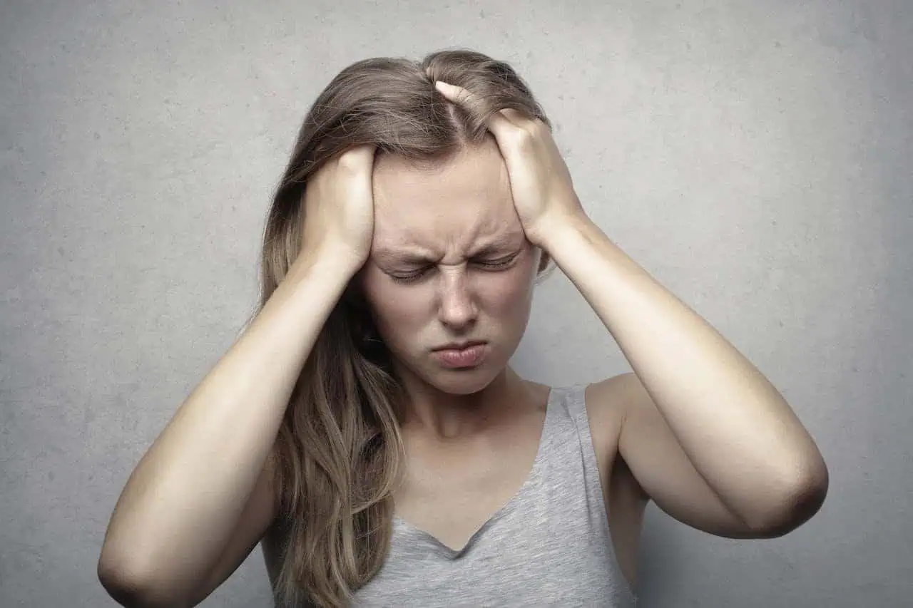 Frustrated woman holding head with both hands, experiencing stress or headache, on neutral background.