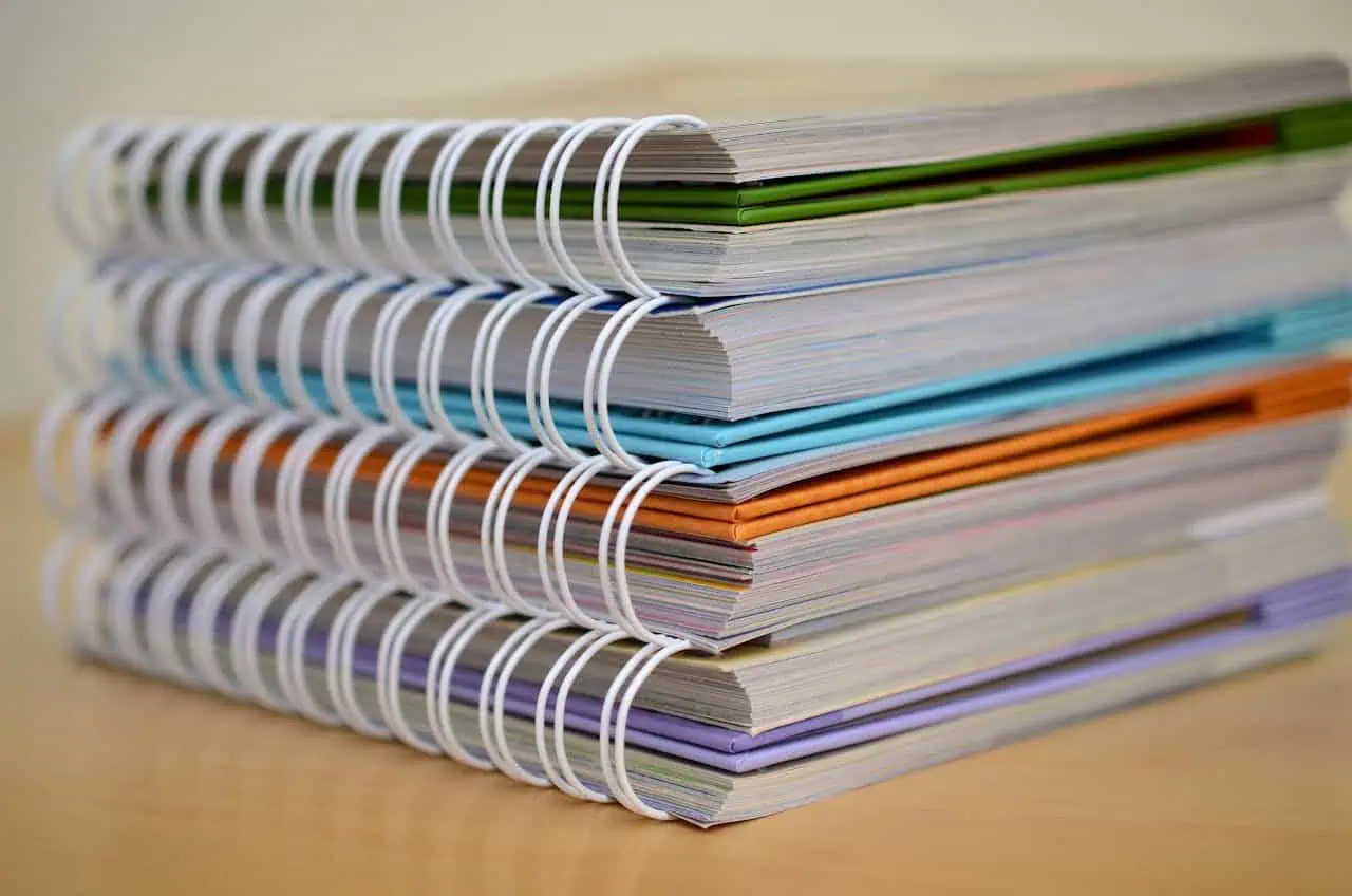 Spiral-bound notebooks with multicoloured covers stacked on wooden surface, used for organisation, planning, or note-taking.