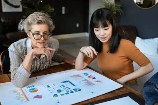 Support worker and young woman discussing data charts and graphs at a table for social work, counselling, or community mental health support.