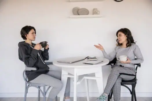 Young woman and girl having a conversation over coffee at a white table, engaging in a supportive discussion, promoting mental health awareness and communication.