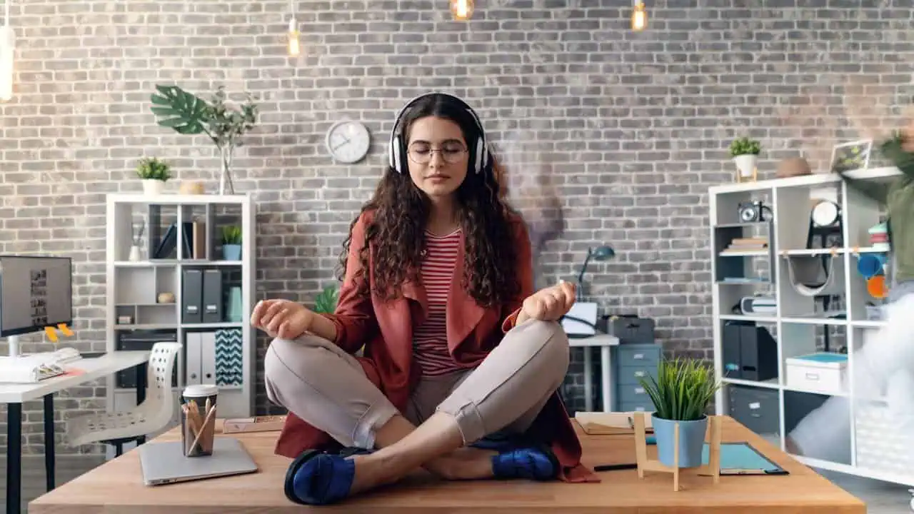 Calm woman meditating at work, practicing mindfulness and stress relief in a modern office setting.