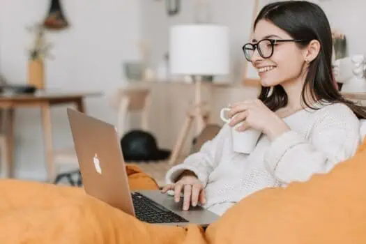 Laptop user smiling working from home using a MacBook in a cosy living room setting.