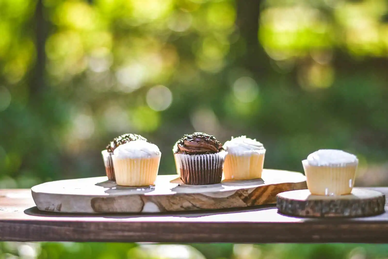 Delicious cupcakes with chocolate and vanilla frosting displayed on a rustic wooden board outdoors, ideal for baking or confectionery photography.