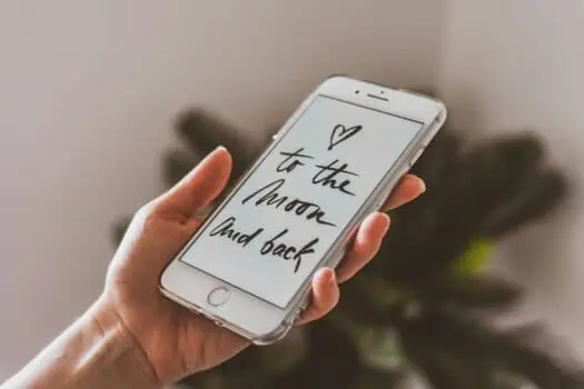 Mobile phone displaying the message "to the moon and back" with a heart symbol, held by a person, representing love and emotional connection.