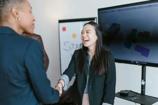 Motivated woman in business attire shaking hands with a colleague during a work meeting, professional networking, female empowerment, successful business interaction, modern office environment.