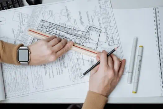 Detailed architectural blueprint of a building, with an architect's hand holding a ruler, working on the technical drawings for construction or renovation projects.