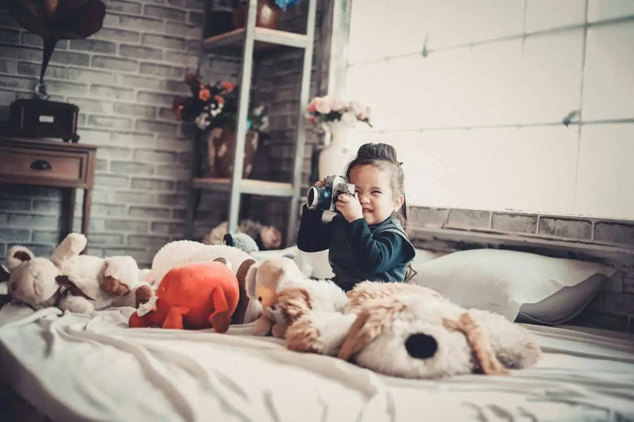 Child playing with plush toys and a camera in a cosy, modern indoor setting, highlighting childhood, playfulness, and comfort.