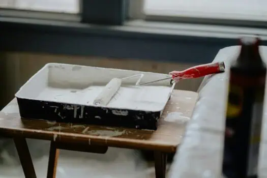Empty paint tray with paint roller and paint bottle on wooden table, room for home renovation or DIY project, neutral background, casual workspace.
