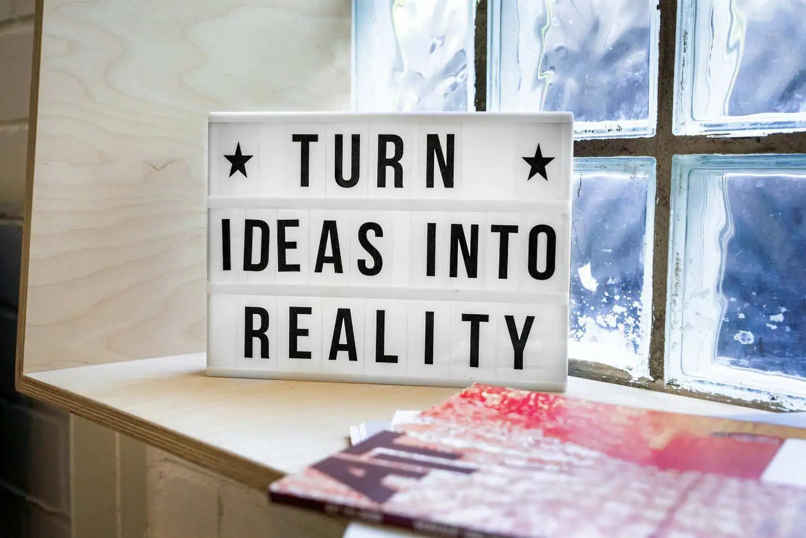 Optimise your ideas with this motivational lightbox sign displayed on a wooden surface near a frosted glass window. Perfect for inspiring creativity, innovation, and positive thinking in a modern workspace.