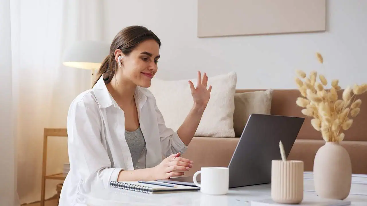 Woman video conferencing with earbuds at home, engaging in online communication or virtual meeting, demonstrating digital connectivity and remote work from the comfort of her living room.
