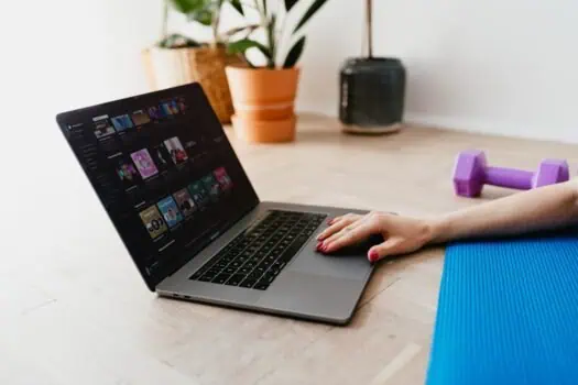 Streaming music on a laptop for relaxation or exercise, with a yoga mat and dumbbells nearby in a home workout setup.