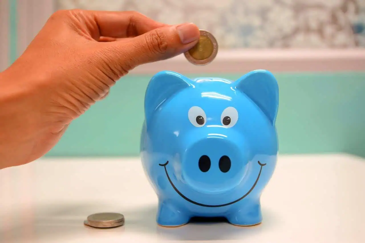 Coin being inserted into a blue piggy bank with a smiling face, promoting saving money and financial education for children.