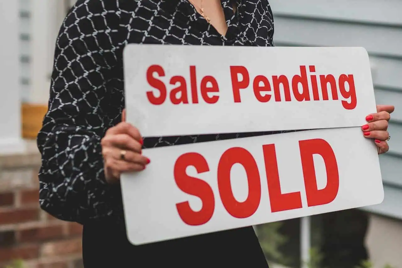 Sale pending and sold real estate sign held by a woman in front of a house.