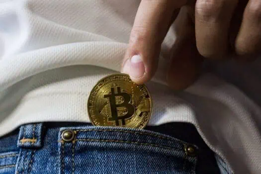Bitcoin cryptocurrency coin being placed into jeans pocket with white shirt; digital finance, blockchain technology, and cryptocurrency investment.