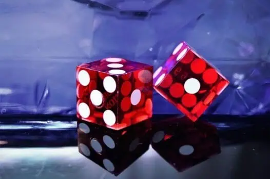 Red and white polka dot dice on reflective surface, vibrant gaming equipment, close-up shot for casino or gaming-related content, dark background with colorful lighting.