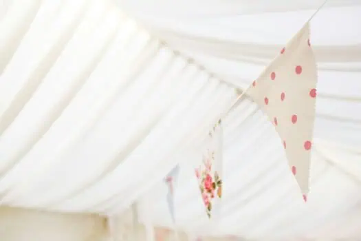 Bright fabric bunting with pink polka dots and floral patterns hanging indoors, decorative banner ideal for celebratory events or community gatherings.