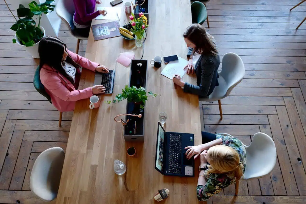 Team of women collaborating in a modern office meeting room with laptops and notebooks, teamwork, professional development, women empowerment, creative workspace.