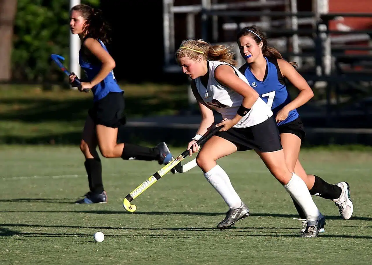 Field hockey match with young female players, athletic women in action, sports children playing hockey, team sport, outdoor field hockey competition, girls in sports uniforms, active sports evening, women athletes in action, field hockey game in progress, women sports team.