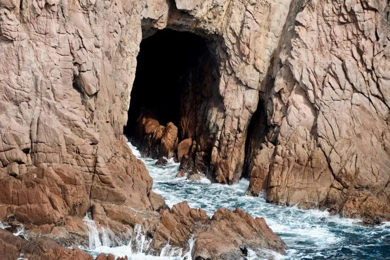 Natural rock formation with sea cave on rugged coastline in Cornwall, UK.
