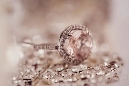A close-up of a silver ring with a large pink gemstone and surrounding smaller diamonds, resting on a sparkling jewelry piece, showcasing elegance and luxury.