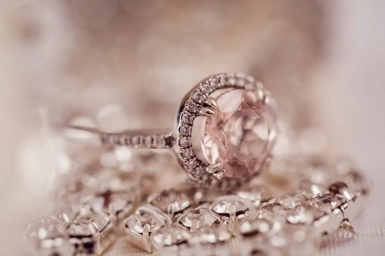 A close-up of a silver ring with a large pink gemstone and surrounding smaller diamonds, resting on a sparkling jewelry piece, showcasing elegance and luxury.
