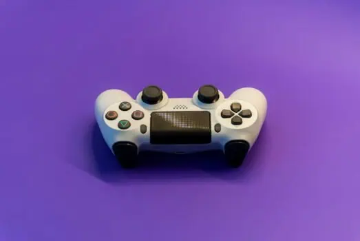 A white gaming controller on a purple background, featuring colourful buttons and a central touchpad, representing gaming, technology, and entertainment.