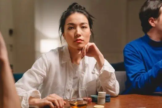 Focused woman in her 30s playing poker at a casino table, with chips and a glass of whiskey. She appears confident and deep in thought, engaging in a poker game or gambling activity.