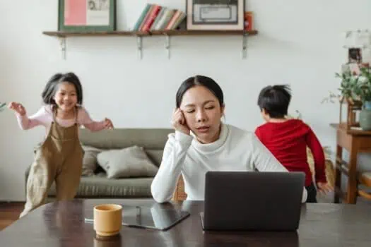 Overwhelmed woman working at home with children, stress, multitasking, juggling family and work, parenting challenges, busy mother with kids, domestic life, family responsibilities, work-life balance, home office setup.
