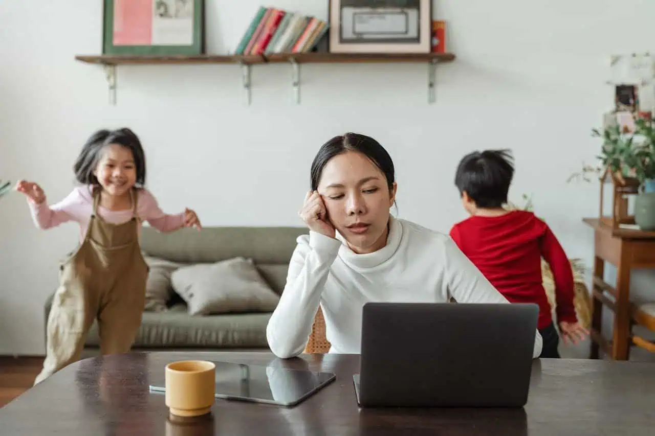 Overwhelmed woman working at home with children, stress, multitasking, juggling family and work, parenting challenges, busy mother with kids, domestic life, family responsibilities, work-life balance, home office setup.