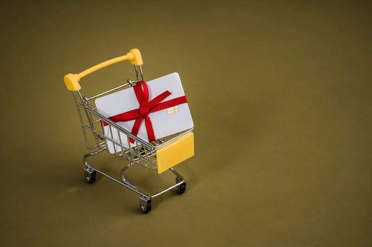 Gift card in a miniature shopping cart with a red ribbon, symbolising online shopping and gift vouchers for mental health support services.