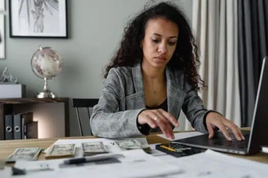 Money management, budgeting, and financial planning concept with woman counting cash on desktop and using calculator for personal finance.
