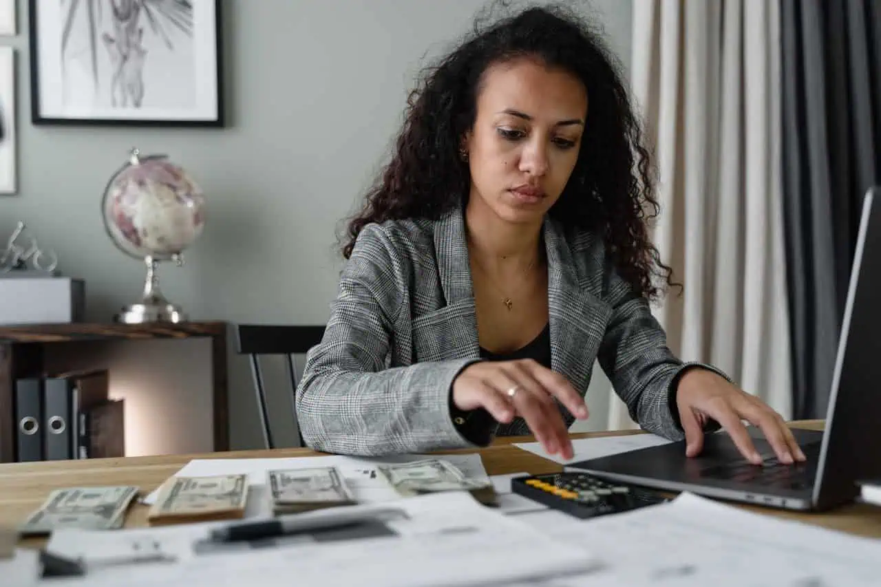 Money management, budgeting, and financial planning concept with woman counting cash on desktop and using calculator for personal finance.