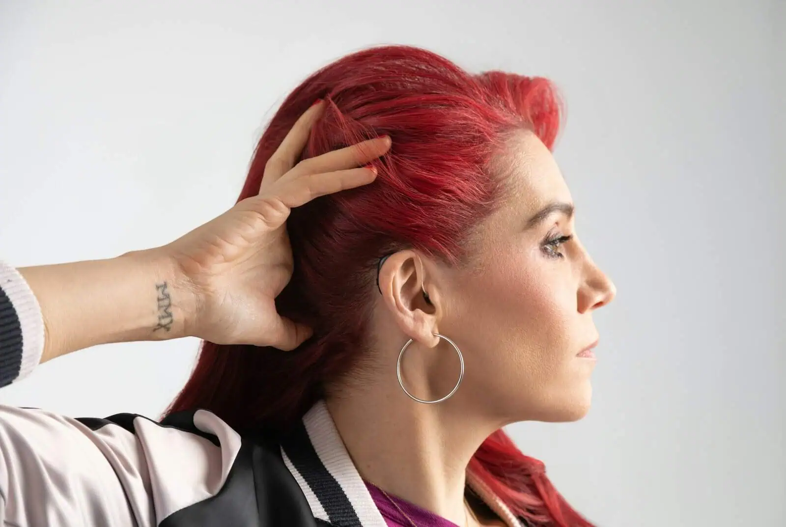 Bright red-haired woman with styled hair, wearing hoop earrings, facing profile in a fashion and beauty context.