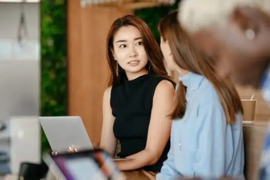 Diverse group of young professional women engaging in a discussion in a modern workspace, highlighting teamwork, collaboration, and workplace diversity.