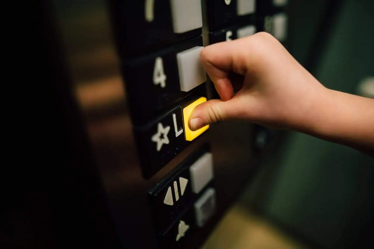 Yellow elevator floor button being pressed by a person's hand in an office building.
