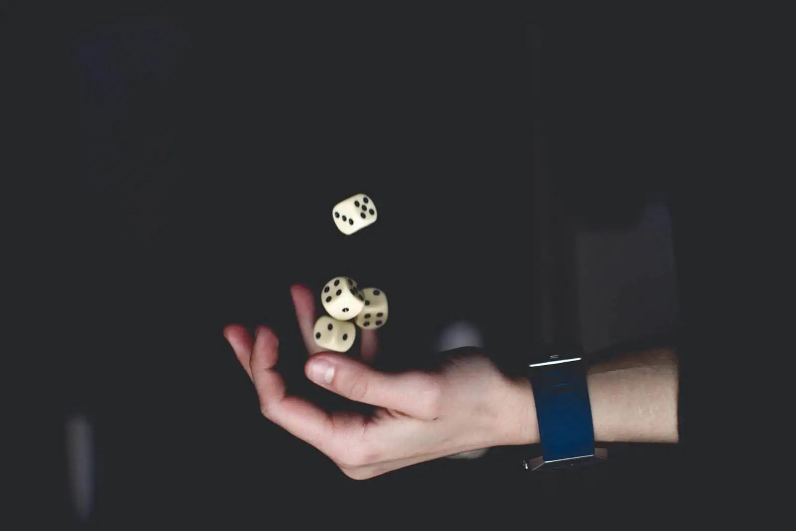 Dice rolling in mid-air with a person's hand supporting the dice, symbolising chance and decision-making, on a dark background, representing games of luck or strategy.