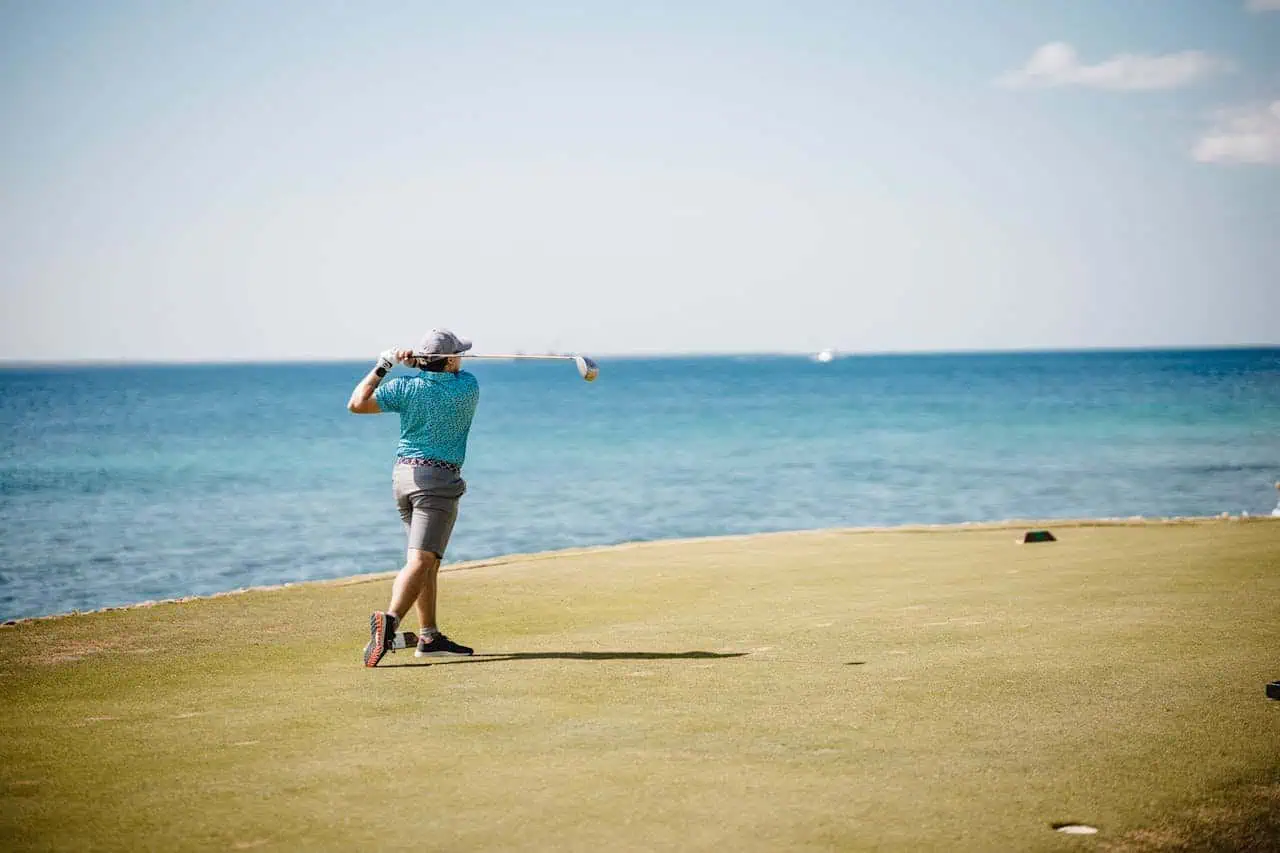 Golf player hitting a shot on a seaside golf course with ocean view, sunny sky, and clear weather, illustrating leisure, golf, and coastal outdoor activities.