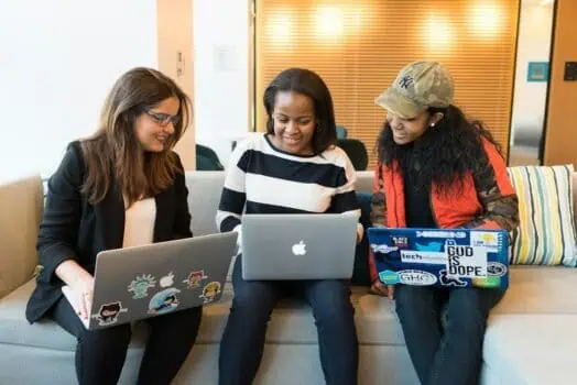 Diversity group of three women working together on laptops in a modern office environment.