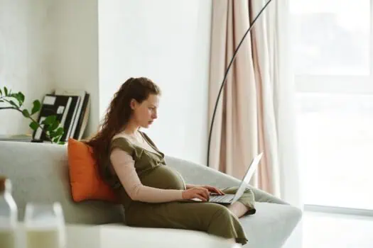 Pregnant woman relaxing on sofa using laptop at home, modern interior, comfortable living space, maternity and remote work, cosy home environment, natural light, casual clothing, parenting and pregnancy.