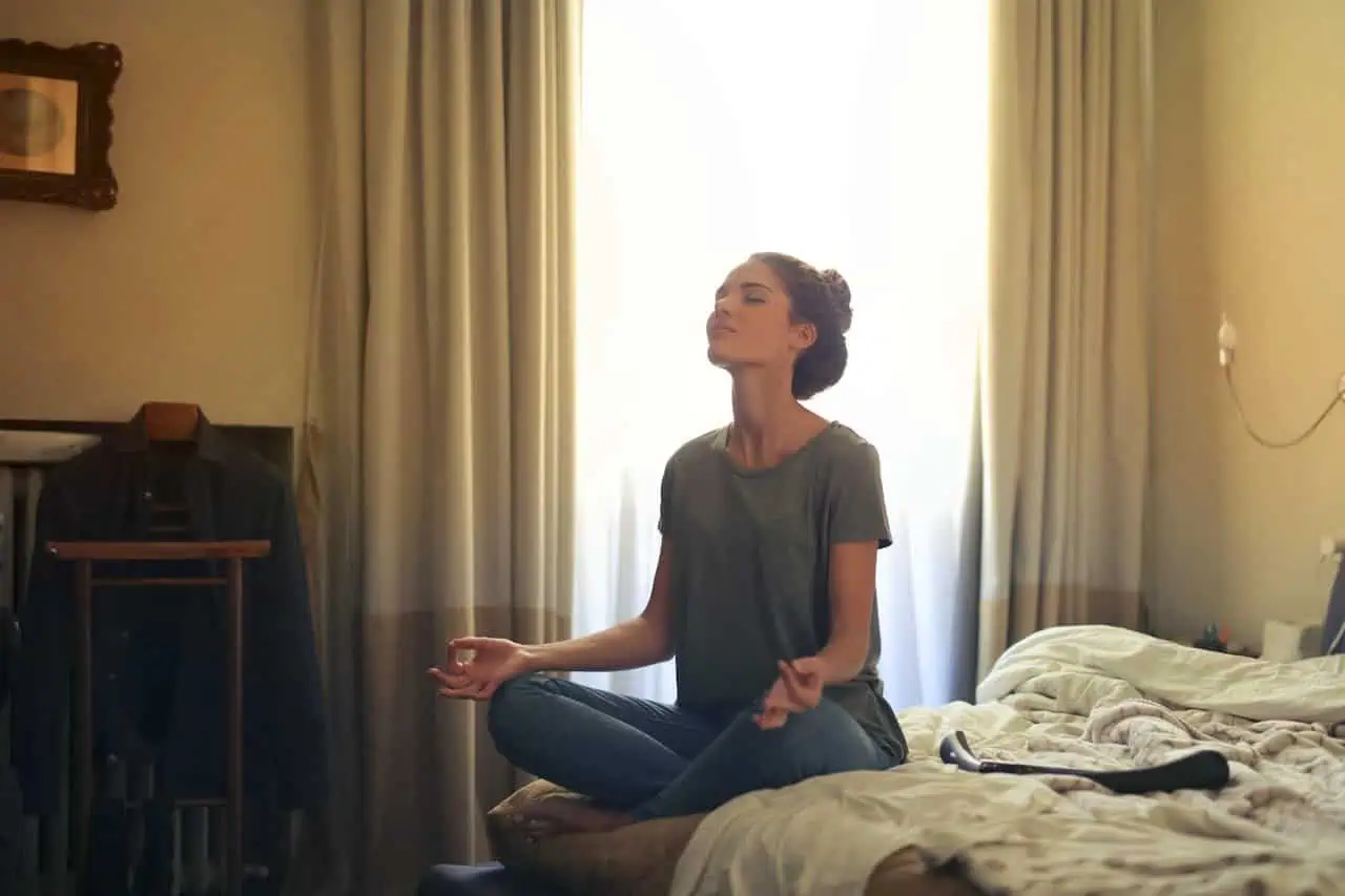 Calm woman practicing meditation in hotel room, mindfulness, relaxation, stress relief, yoga, wellness, mental health, tranquility, self-care, indoor relaxation.