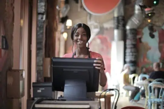 Smiling waitress standing behind a restaurant counter with a computer at Prowess restaurant in the UK.
