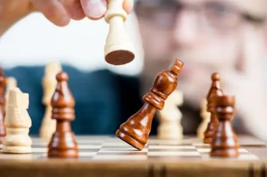 Growing chess game strategy with a hand moving a white queen piece on a wooden chessboard. Focus on mental skills, problem-solving, and strategic thinking for chess players.